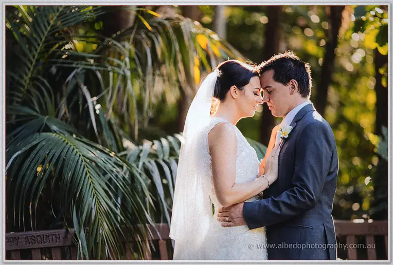 Foreheads touching, the couple shares a quiet moment in dappled garden light.