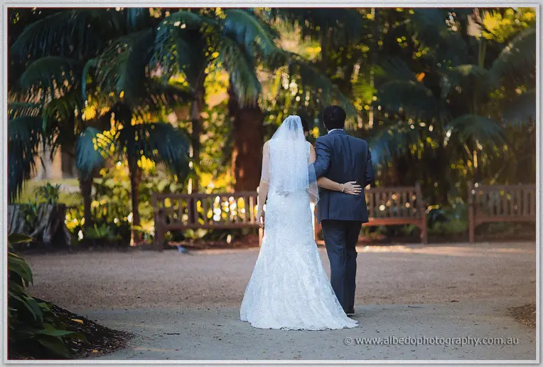 Arm in arm, the newlyweds wander away down a garden path toward the shaded benches.