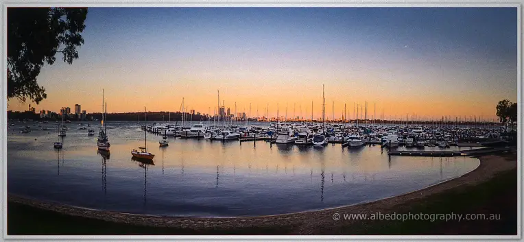 Wide dusk view of the Matilda Bay foreshore, yachts on glassy water under an amber sky.