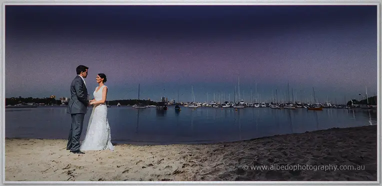 Wide dusk scene on the bay's quiet beach, the couple face to face on pale sand under a violet sky.