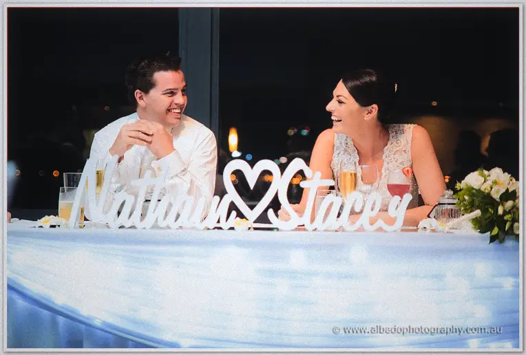 Giggling beneath their white name cut-out, the couple trade looks across the bridal table.