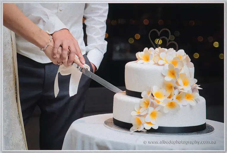 Stacey and Nathain cut their frangipani-topped wedding cake against night lights at Matilda Bay.