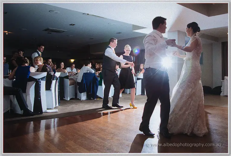 Stacey and Nathain dance across the timber floor as wedding guests watch from white-clothed tables.