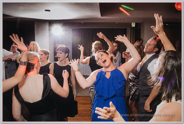 A guest in a blue halter dress sings along, arms flung up, on the packed dance floor.