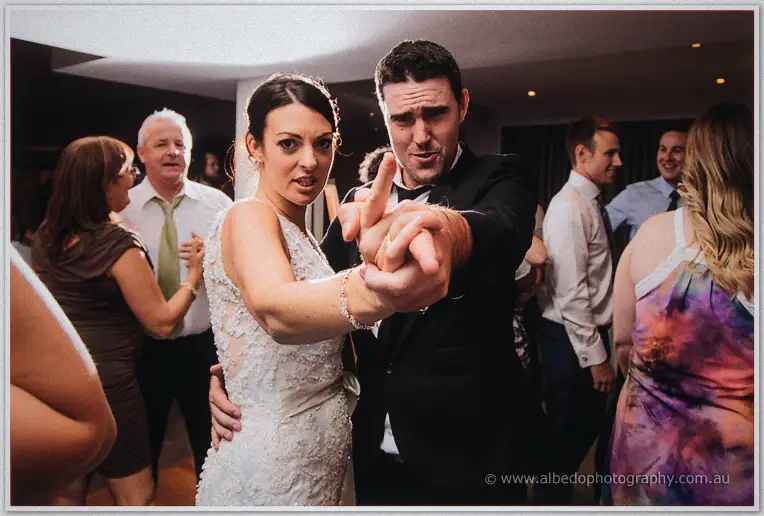Stacey points at the camera while dancing with a suited guest among the crowd.