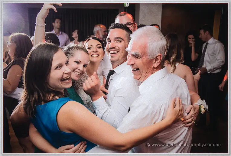 Friends and family huddle close, laughing, as they dance together at the reception.
