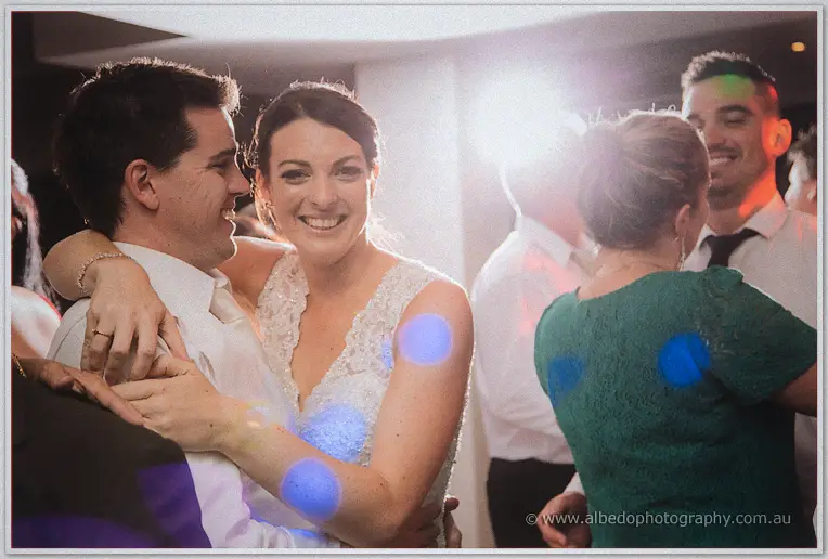 Stacey hugs Nathain from behind, both beaming, under blue party lights on the dance floor.