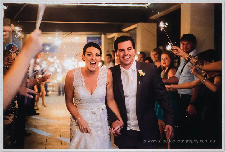 Stacey and Nathain walk hand in hand through a sparkler-lined send-off at night.