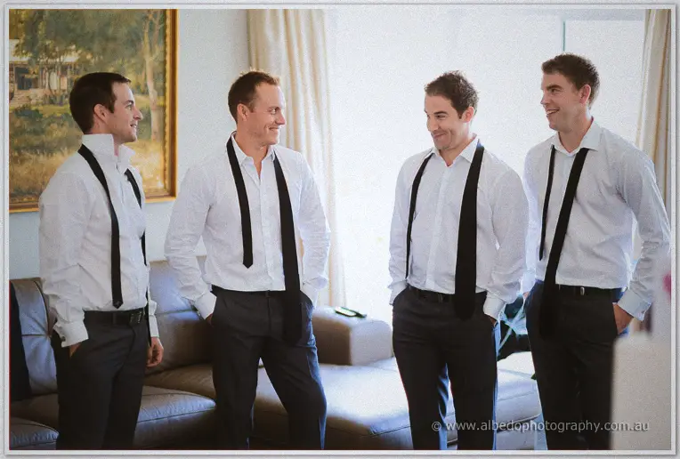 Mitch and his groomsmen laugh in the lounge room, white shirts open with black ties still hanging undone