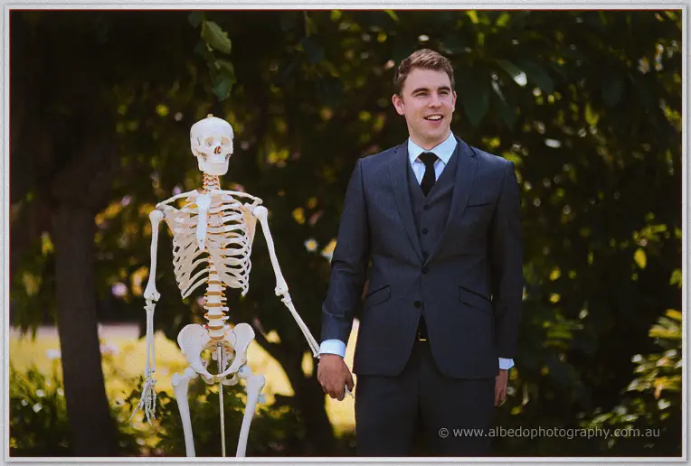 Mitch grins as he holds hands with a toy skeleton in the leafy garden for a playful portrait