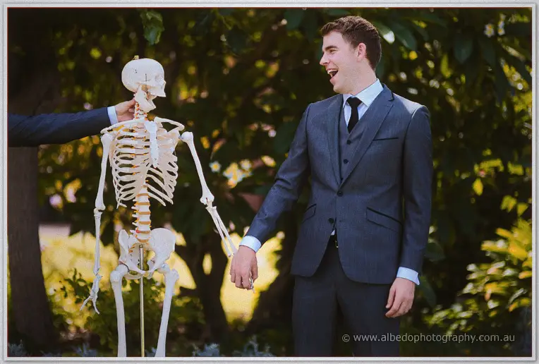 Laughter as a groomsman steadies the skeleton while Mitch clasps its hand among the greenery