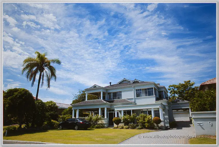 Bright morning sun on a grand white two-storey home with palm tree and manicured lawns before the wedding