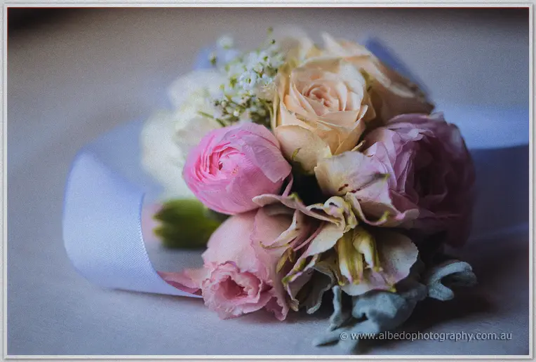 Close-up of a pastel rose and ranunculus wrist corsage trailing soft blue ribbon