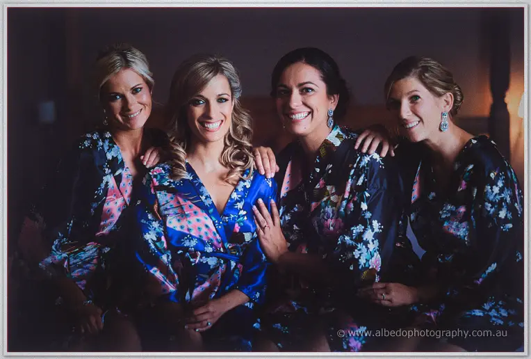 Cristina and her bridesmaids beam together in matching dark floral robes, arms around each other