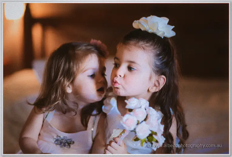Two little flower girls pull silly faces, one clutching her posy of pink roses