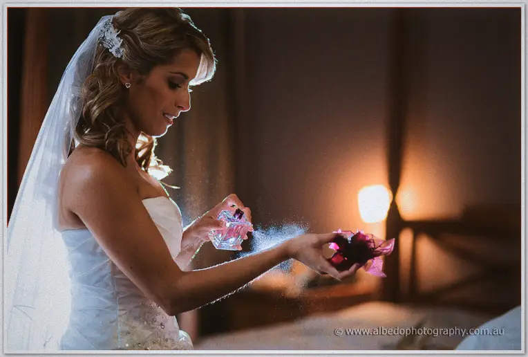 Veiled Cristina spritzes perfume onto a posy in the amber lamplit bedroom