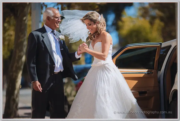 Cristina holds her father's hands and laughs beside the open limousine door
