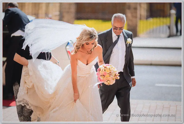 Father escorts Cristina past the bluestone wall toward the basilica doors