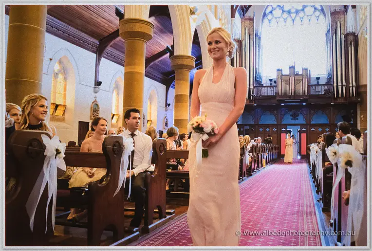 Bridesmaid in blush walks the basilica aisle past ribbon-tied pews