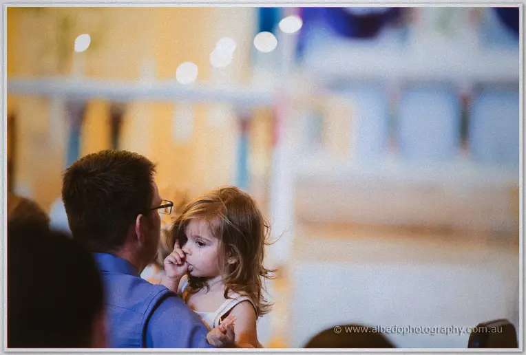 A little girl rests against her father's shoulder, thumb in mouth, amid the hush of the basilica congregation