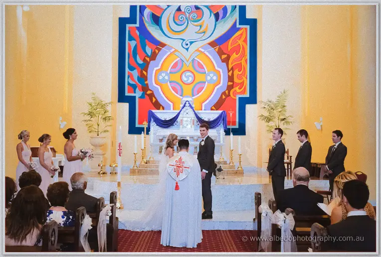Wide view of Cristina and Mitch at the sanctuary before the priest and a colourful painted reredos