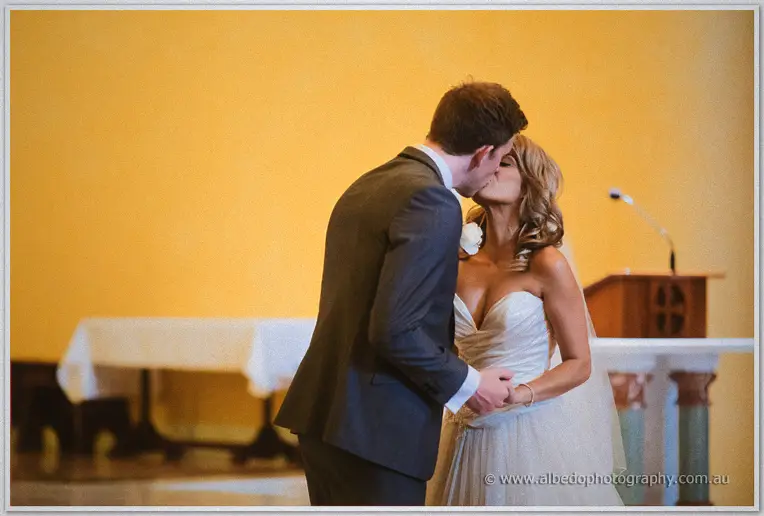 First kiss at the basilica altar, Mitch dipping toward Cristina against a glowing ochre wall