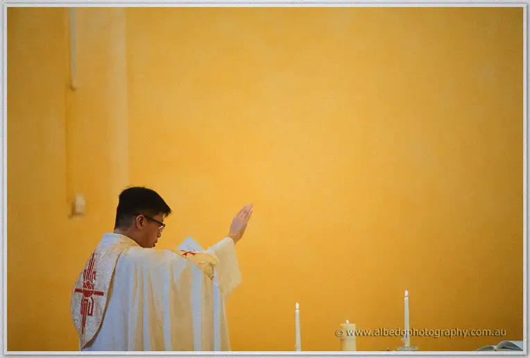 The priest raises his hand in blessing, small and still against the vast golden wall of St Patrick's