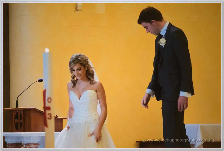 Cristina smooths her gown beside Mitch on the altar steps, both casting playful downward glances