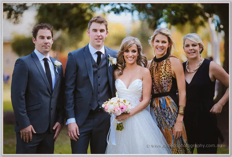 Cristina and Mitch pose with friends in the park, her pink bouquet bright against soft green bokeh