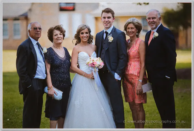 Cristina and Mitch flank their smiling parents on the lawn in low golden-hour light