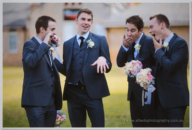 Groomsmen ham it up on the lawn, clutching bouquets and feigning shock as Mitch holds out his ring hand