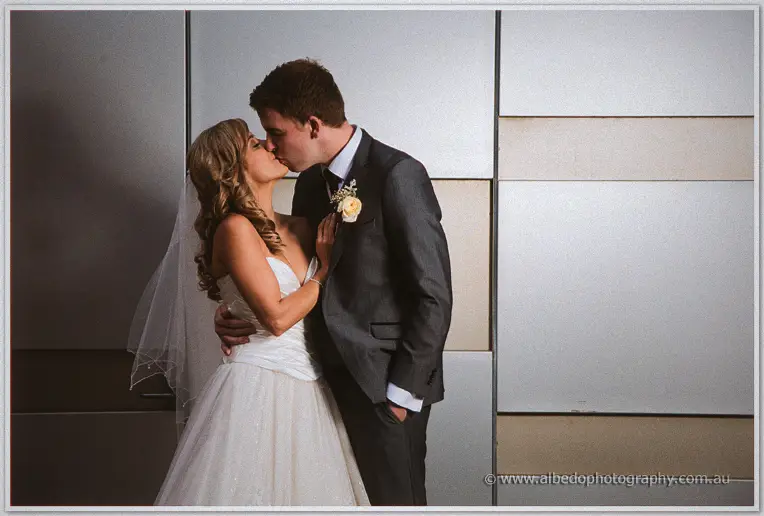 Cristina kisses Mitch against a sleek silver paneled wall, veil falling behind her gown