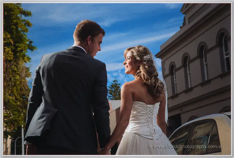 Low-angle view of Cristina and Mitch strolling hand in hand beneath a deep blue city sky