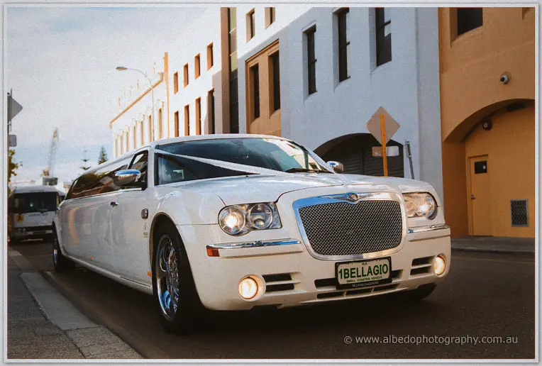 White stretch limousine with a ribbon on its bonnet waits on a quiet city street in afternoon light