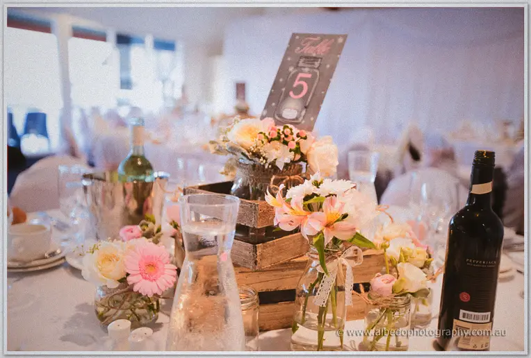 Rustic crate centrepieces hold pink and cream blooms beside wine and a chalkboard table number five