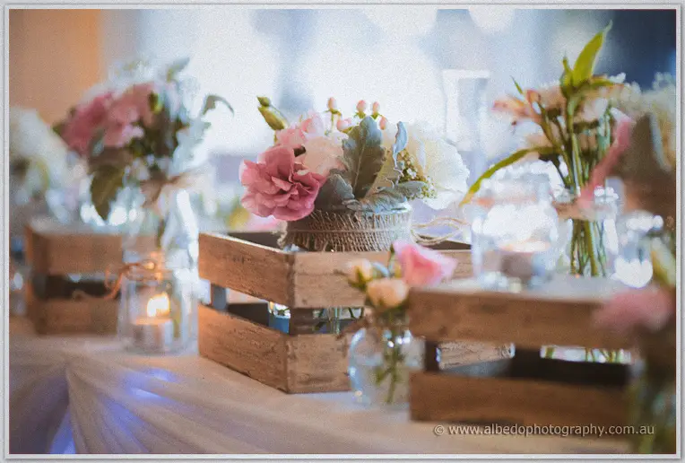 Pastel posies in twine-wrapped jars sit in wooden crates beside glowing candles on the bridal table