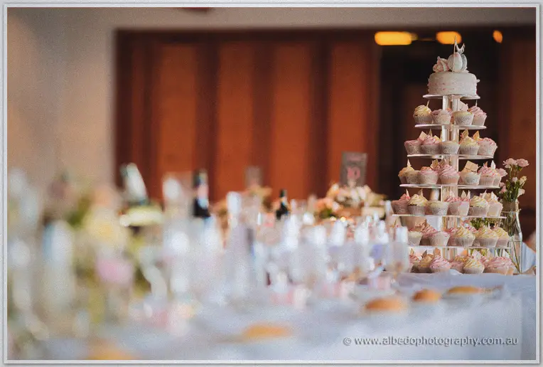 A tiered cupcake tower crowned with a small cake rises above the softly blurred reception tables