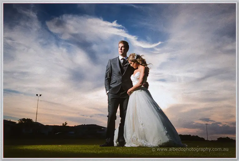 Mitch stands with a hand in his pocket as Cristina leans on his shoulder under dramatic dusk clouds