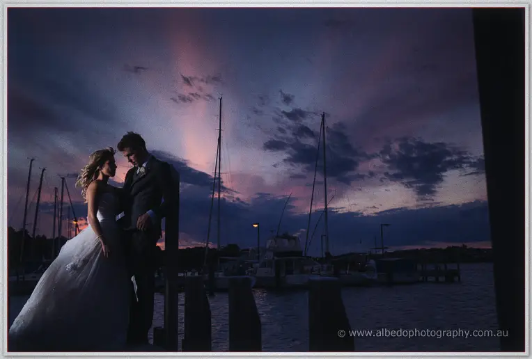Cristina and Mitch embrace on the marina jetty beneath a pink twilight sky at East Fremantle Yacht Club
