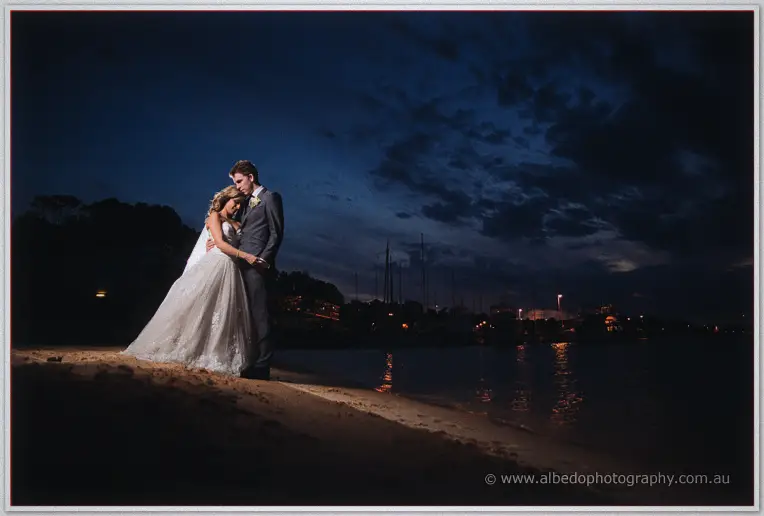 Mitch holds Cristina close on a darkened foreshore, city and marina lights glinting across the river