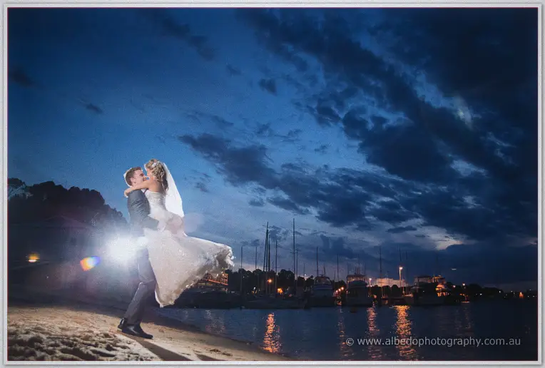 Mitch sweeps Cristina off her feet on the sand, flash flaring against the deep blue evening sky