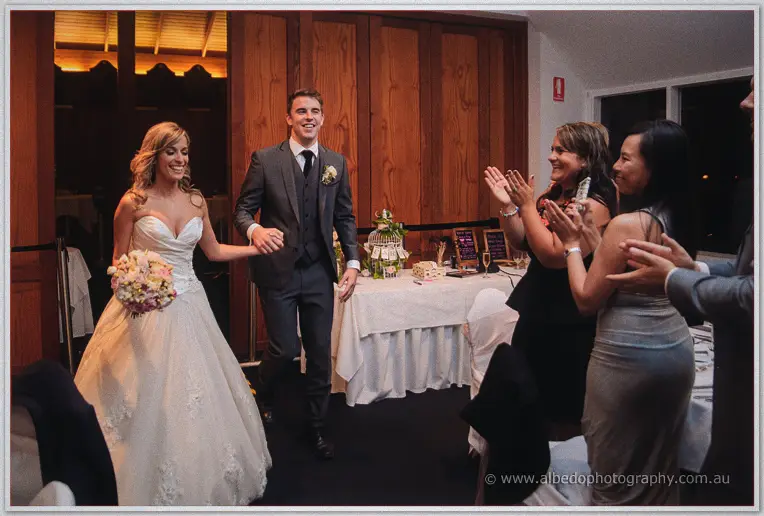 Newlyweds walk hand in hand into the timber-lined reception room while guests rise clapping