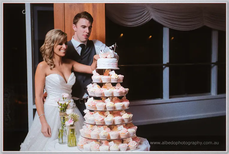 Cristina steadies the cupcake tower's top cake as Mitch wraps an arm around her at the reception