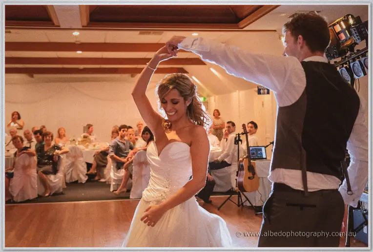 Mitch twirls Cristina, her gown flaring, as guests and a guitarist look on in the yacht club hall