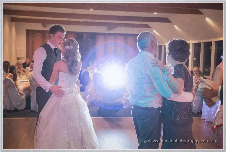 The newlyweds dance close while an older couple spins nearby under a flare of disco light