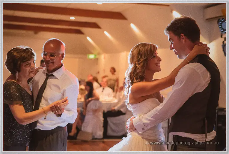 Cristina clings to Mitch's shoulders mid-dance as guests, including an older couple, swirl nearby