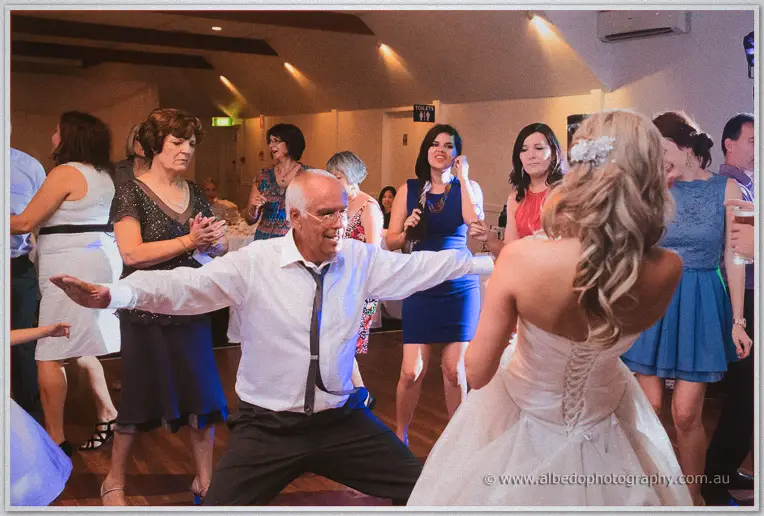 An older guest dances wide-legged with arms flung out as Cristina laughs and the crowd claps