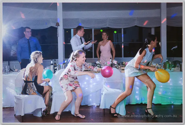 Women clutch balloons mid-game on the dance floor while friends cheer beside fairy-lit tables