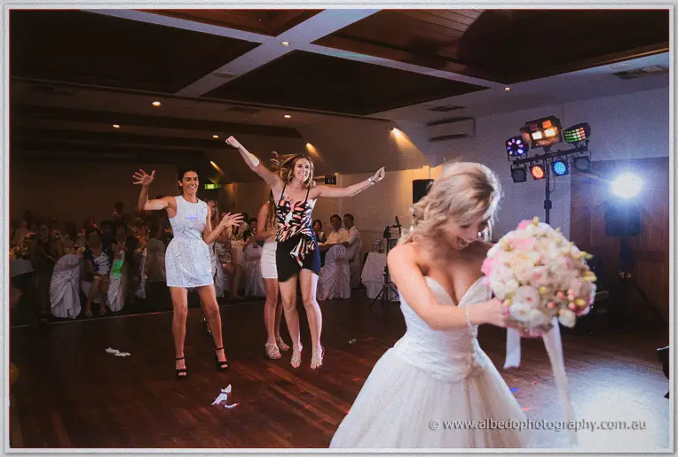 Cristina grips her bouquet as two guests leap and dance behind her on the packed floor