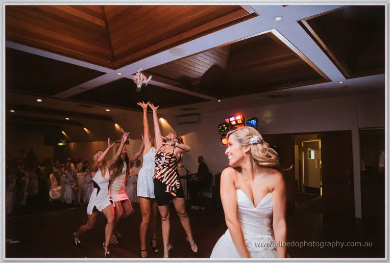 Cristina tosses her bouquet skyward while guests leap, arms outstretched, to catch it